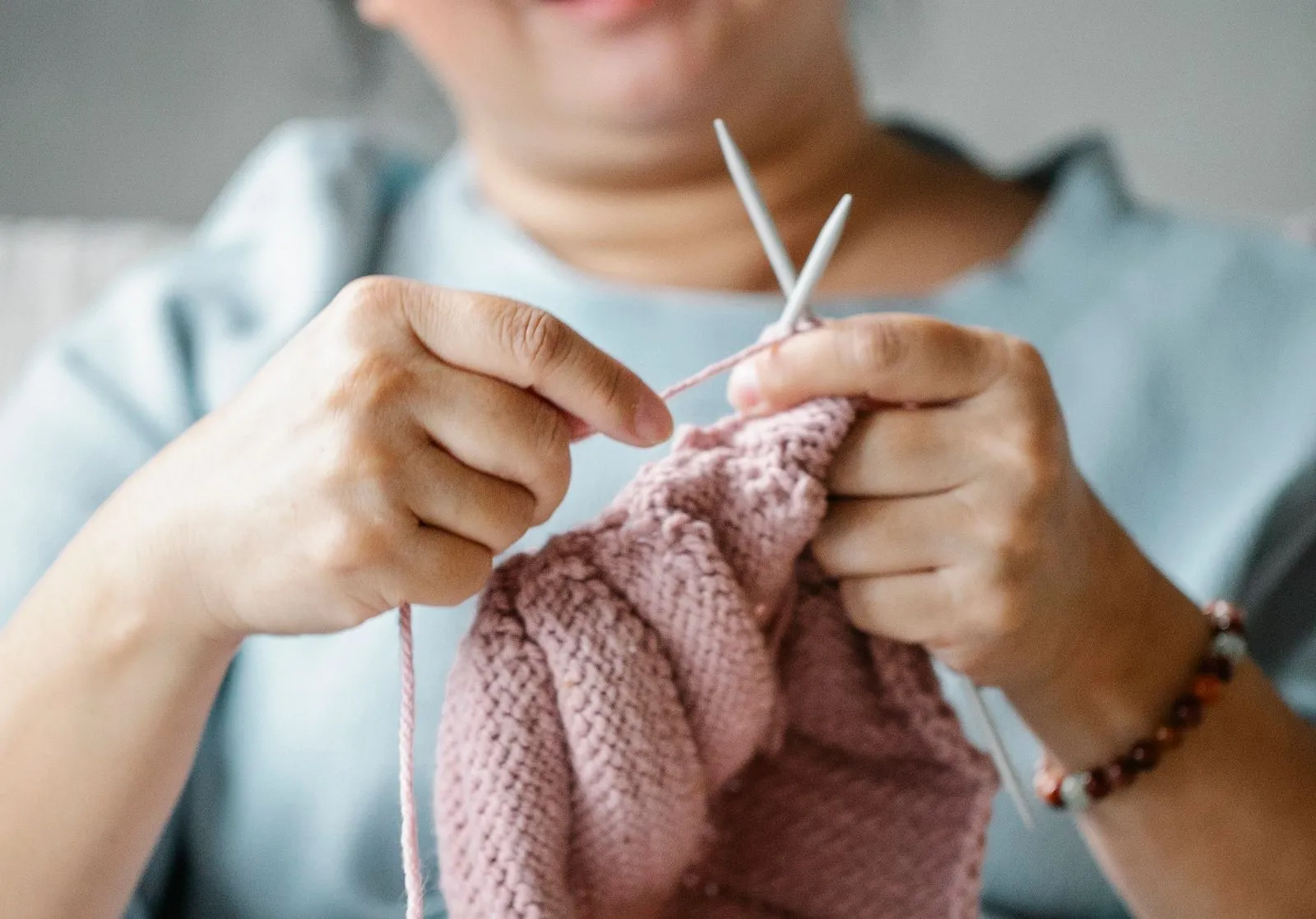 Crop mature female resting at home and knitting with pink yarn and needles